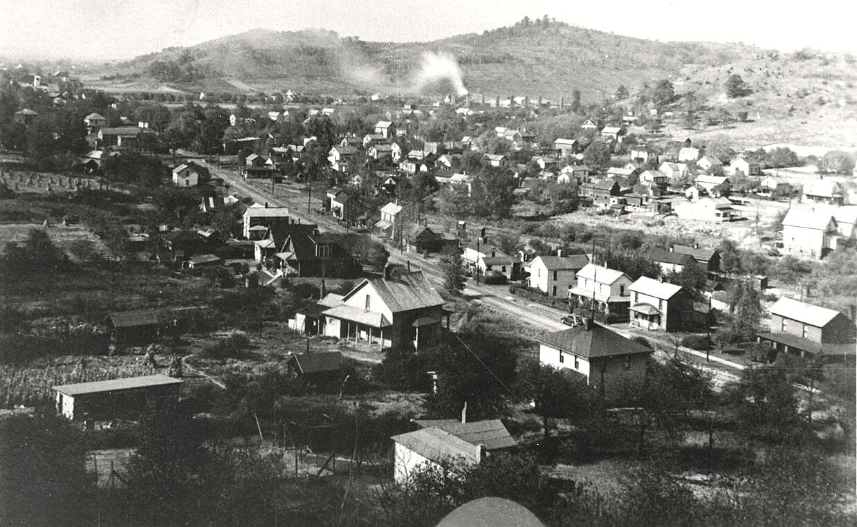 A historical panoramic photograph of the Village of Midvale, Ohio, taken from the surrounding hillside, showing rooftops of homes and dirt streets in the Tuscarawas River valley with hills rising in the distance.